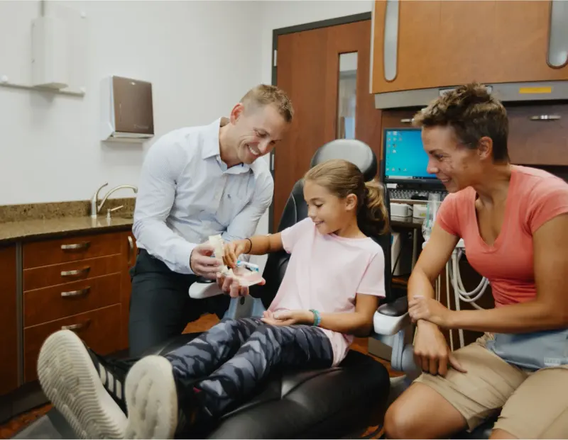 Dr. David Gallup laughing with a young patient and her mom in a Hilltop treatment room
